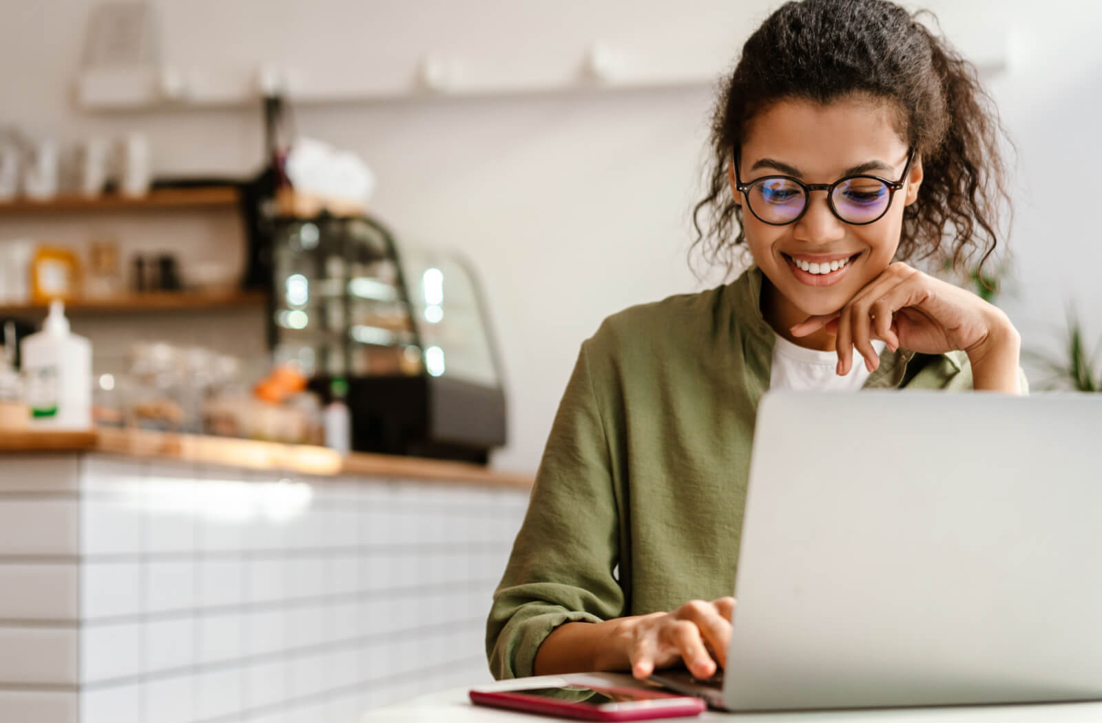 A young adult female student is smiling, wearing Neurolens glasses while doing homework on her computer laptop