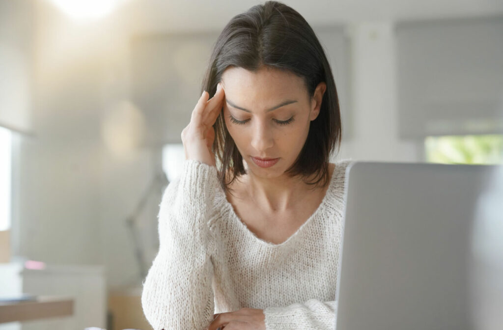 A young woman sitting in front of her computer is experiencing headaches and digital eye strain