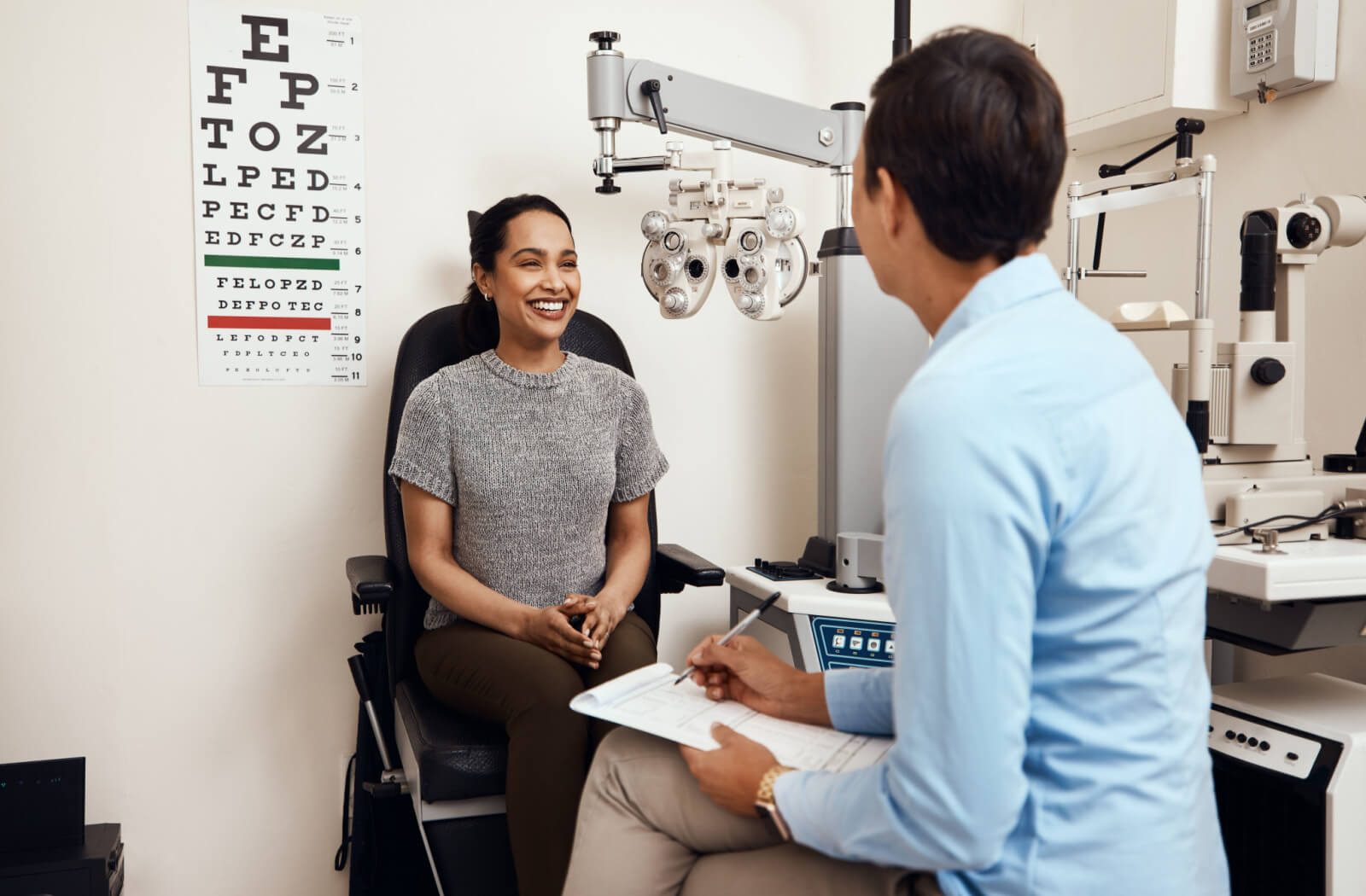 A young woman sitting in an optometrist's office and smiling at her eye doctor