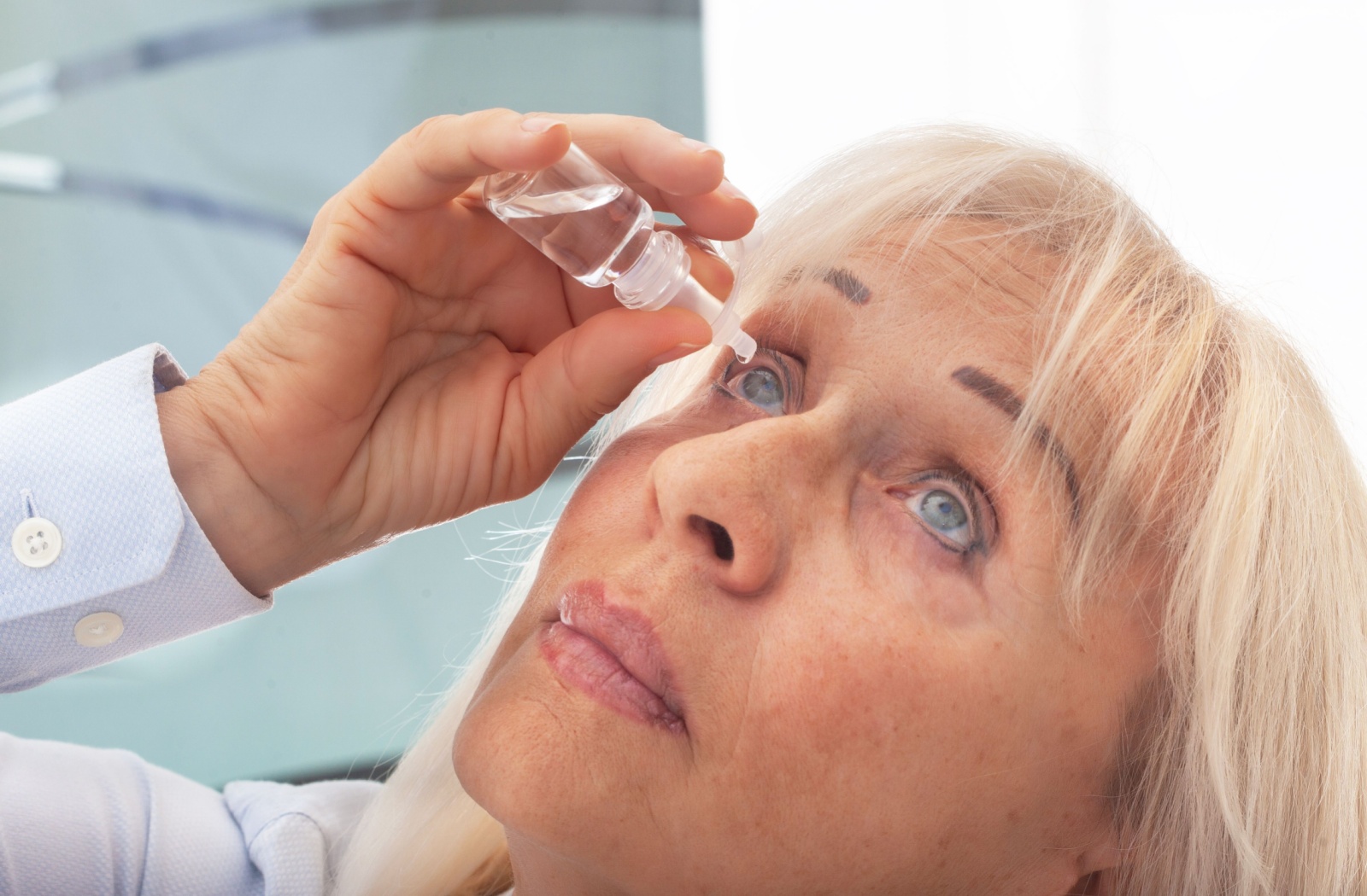 A woman applying eyedrops to alleviate dry eye symptoms.