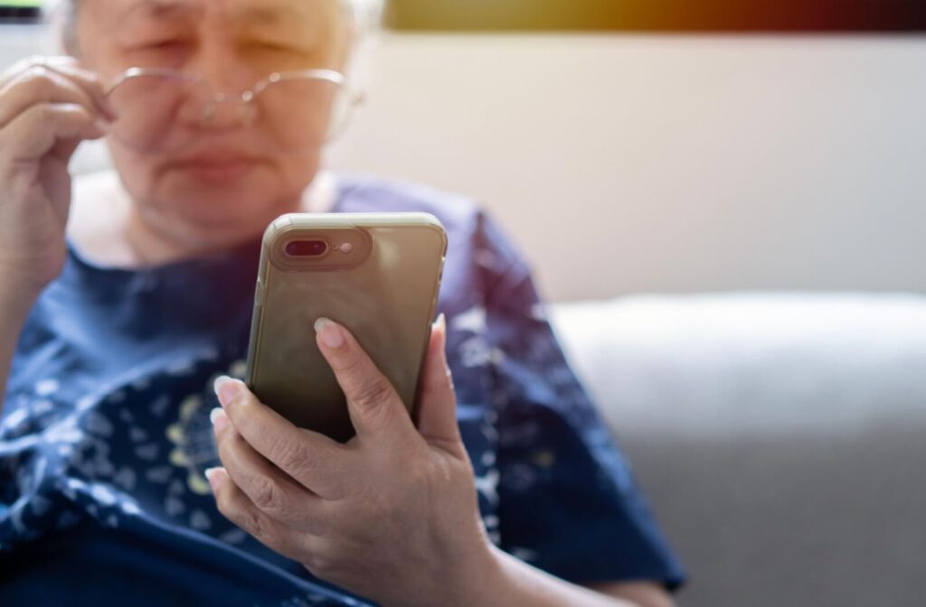 An older adult holding a smartphone struggles to read small text on the screen due to age-related macular degeneration.