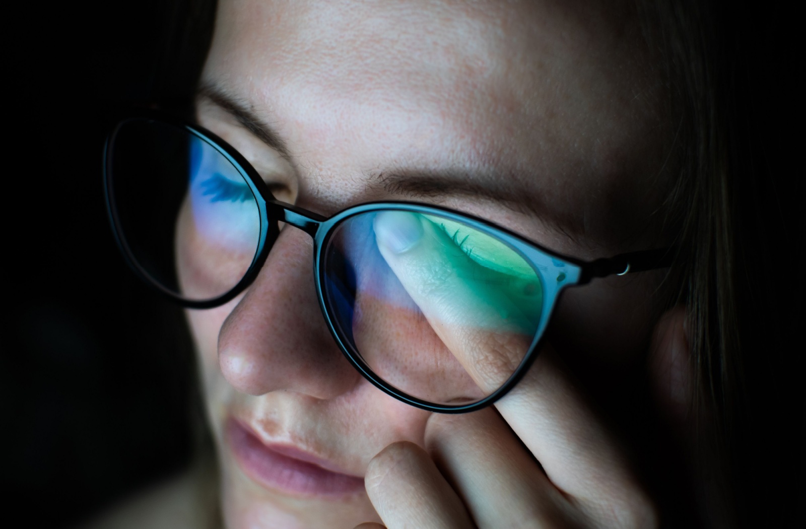 Someone wearing glasses rubs their eye beneath their glasses.