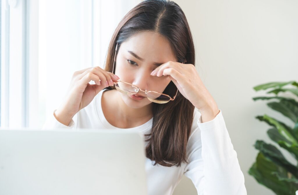 Someone with dry eyes from working on a computer removes their glasses.