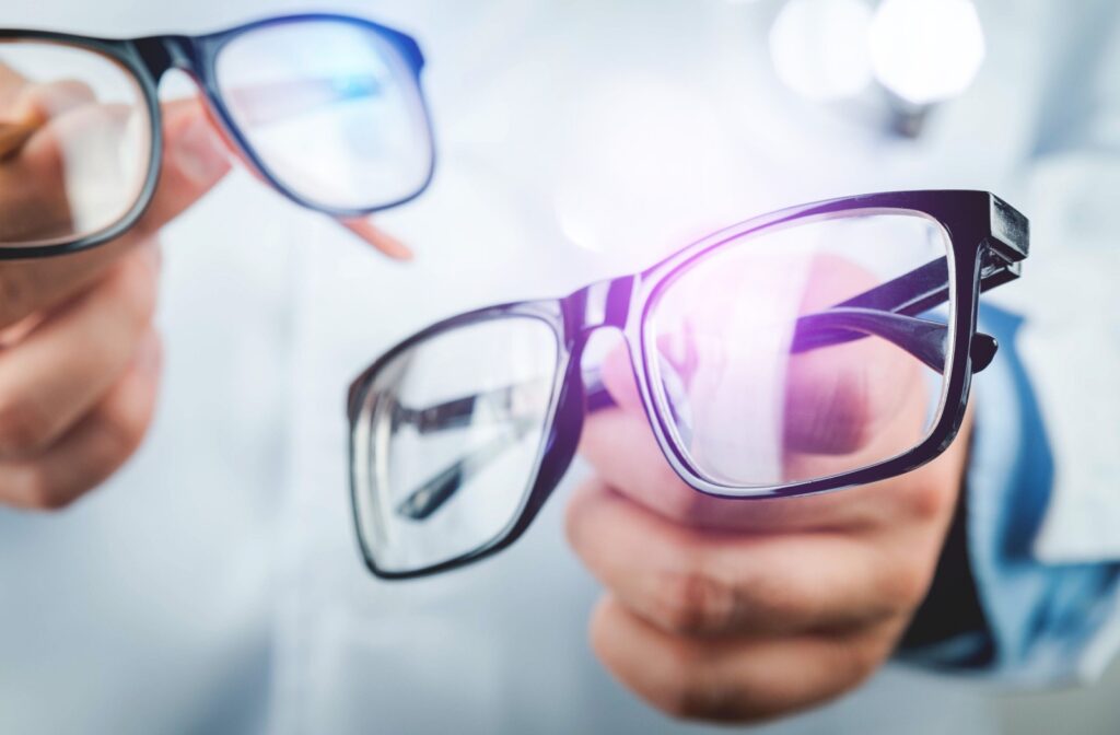 An optometrist holds up two pairs of black eyeglasses, one with traditional lenses and one with Neurolens lenses.