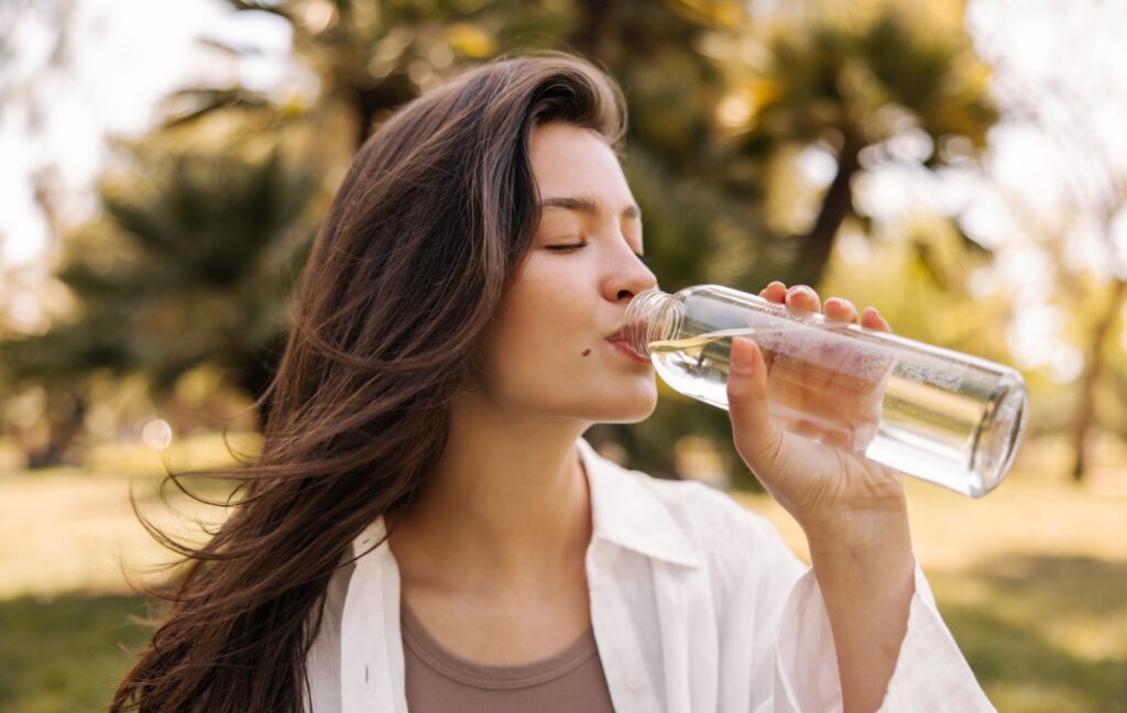 A person drinks from a water bottle to stay hydrated and promote eye health during a warm, dry day.