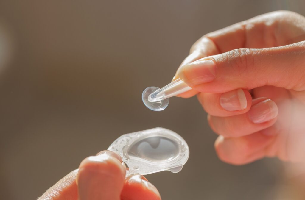 A close up of someone using contact lens tweezers to hold up a contact lens out of its original packaging